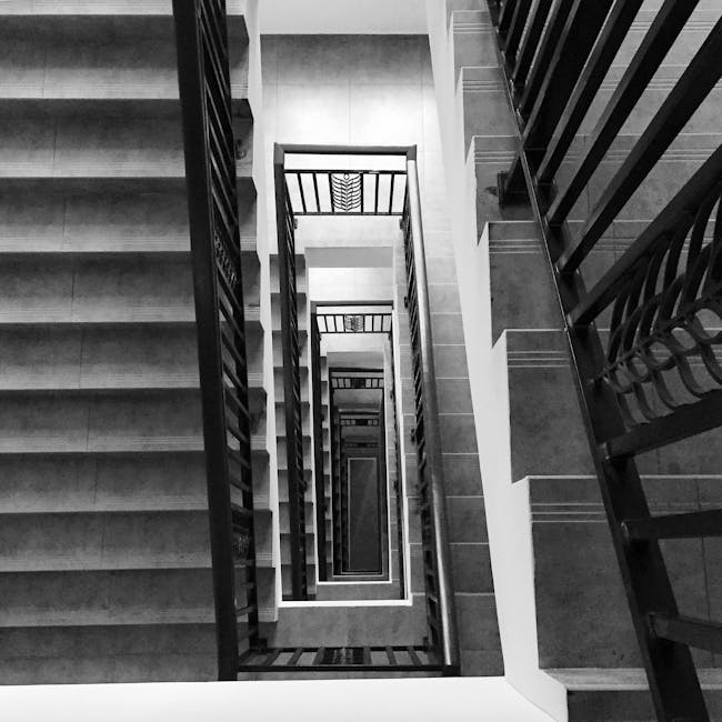 A black and white photograph taken from the top of a multi-story staircase looking downward, revealing the repetitive pattern of landings and railings as the stairwell extends floor by floor. The stai
