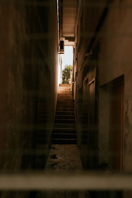 A black and white photograph taken from the top of a multi-story staircase looking downward, revealing the repetitive pattern of landings and railings as the stairwell extends floor by floor. The stai